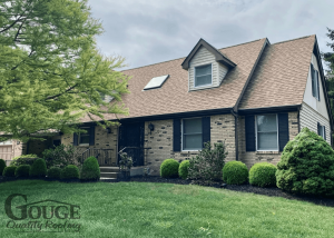 angled view of small residential brick home with asphalt shingle roofing and gouge logo in bottom left corner