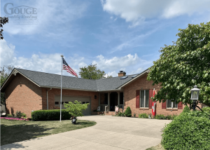 front view of driveway leading to brick home with asphalt shingle roofing; gouge logo in upper left corner