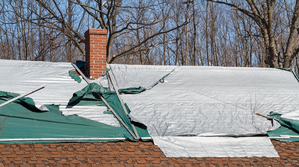 Leaking house roof covered in tarp in need of roofing repair. Room for copy text.