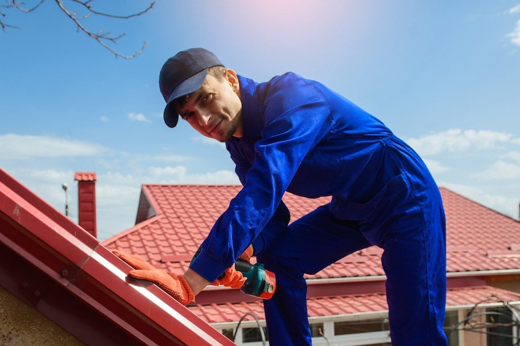 Young man worker in blue overall fix a metal tile roof; diy metal roof