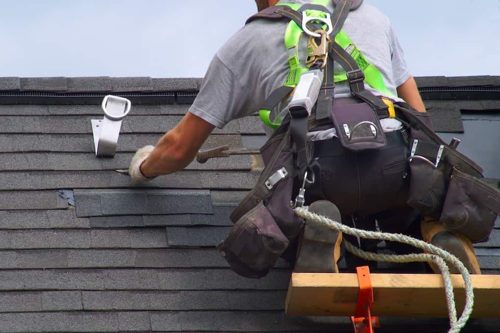 professional roofer wearing safety harness on roof while showing how to find a roof leak
